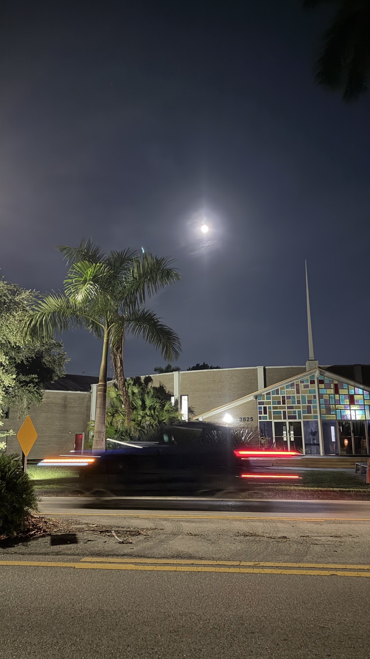 A bright full moon above buildings and trails of car lights